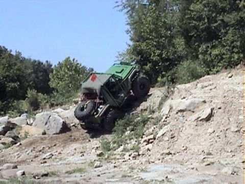 1992 Ford Bronco - A green open-top trail rig with a chopped body, roll cage, spare tire on the rear and big knobby tires crawls nose-down off a rocky ledge a…