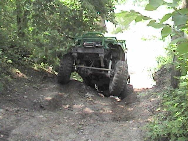 Green caged 4x4 buggy climbing a dirt ledge with undercarriage and axle exposed
