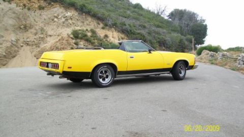 1973 Mercury Cougar - A yellow convertible with a black stripe runs along the lower body, parked on a paved road.