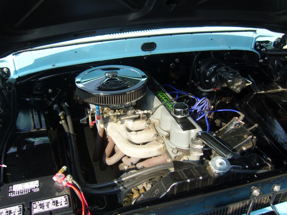 Engine bay with chrome air cleaner, V8 engine, blue spark plug wires, and battery