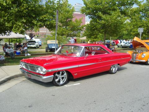 2007 Ford Mustang - A bright red 1964 Ford Galaxie 500 coupe is parked at a car show, with other vehicles and spectators in the background.