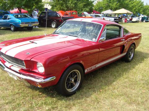 2007 Ford Mustang - A classic red 1965 Ford Mustang GT350, distinguished by its white racing stripes, is displayed at an outdoor event.