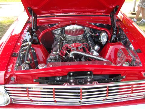 2007 Ford Mustang - The engine compartment of a vintage red car is open, revealing a polished V8 engine and intricate wiring.