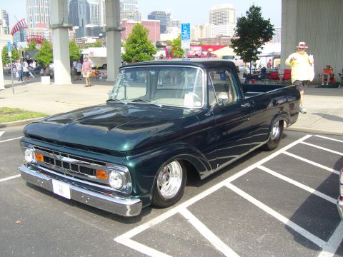 2007 Ford Mustang - A dark green 1966 Ford F-100 pickup truck is parked at an outdoor event with a city skyline in the background.
