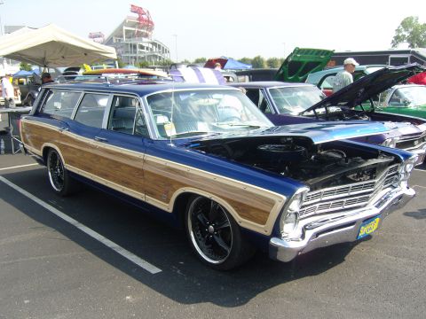 2007 Ford Mustang - Station wagon with wood paneling and surfboards on the roof is displayed at an outdoor car show.