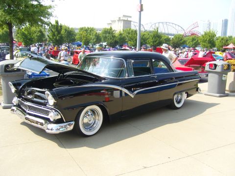2007 Ford Mustang - Black 1955 Ford Fairlane Crown Victoria at a car show, hood up, with other vehicles and people in the background.