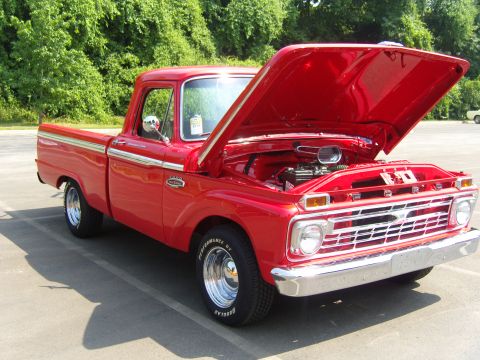 2007 Ford Mustang - A bright red 1965 Ford pickup truck is parked outside with its hood open, revealing the engine compartment.