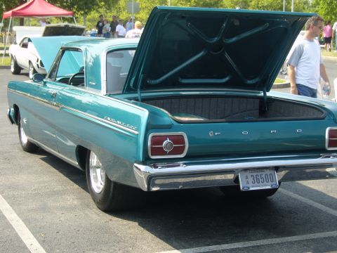 2007 Ford Mustang - A teal 1965 Ford Fairlane sedan is parked with its trunk open, showing its interior and a glimpse of another car behind it.