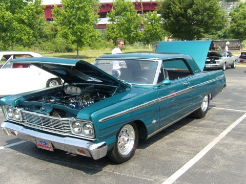 2007 Ford Mustang - A teal 1965 Ford Galaxie is displayed with its hood open, revealing the engine bay. Another car is visible in the background.