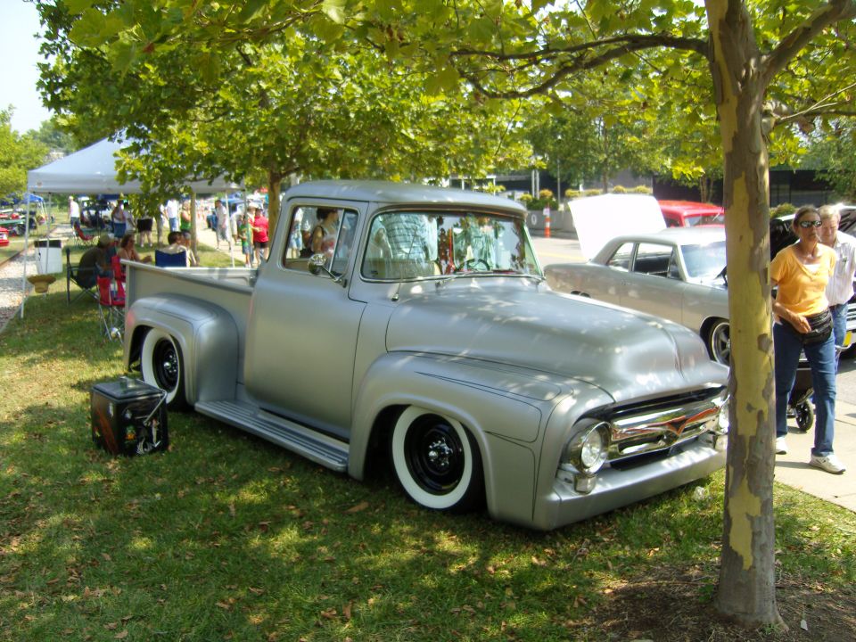 Silver 1956 Ford F-100 pickup truck with wide whitewall tires, lowered suspension, and custom grille