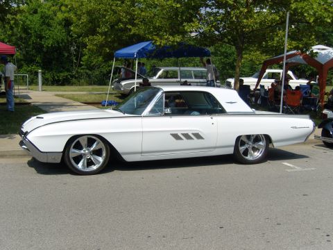 2007 Ford Mustang - A classic white Ford Thunderbird is displayed at an outdoor event with tents and other vehicles in the background.