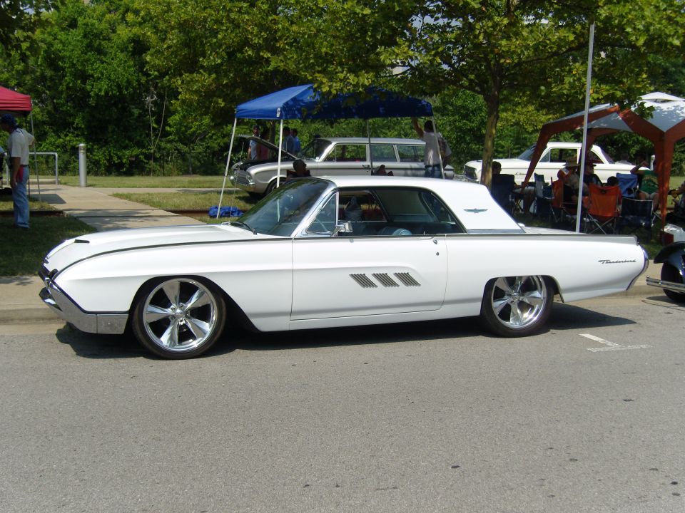 White 1961 Ford Thunderbird coupe with chrome wheels and side vents parked on asphalt