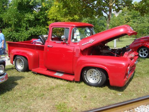 2007 Ford Mustang - This red 1956 Ford F-100 pickup truck is displayed with its hood open, revealing the engine. Text is visible on the tires.