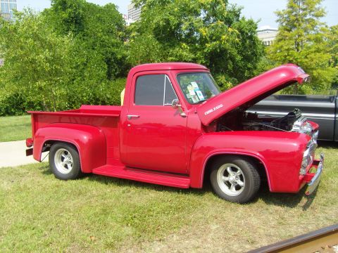 2007 Ford Mustang - Classic red Ford F-100 pickup truck, hood up, at an outdoor event. Another truck is partially visible.