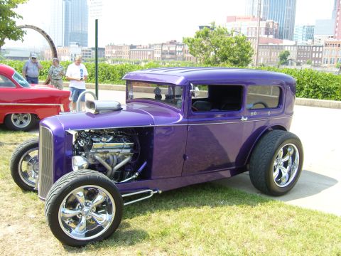 2007 Ford Mustang - A custom purple sedan with a large engine sits on grass, with a red car and city buildings in the background.