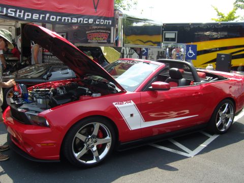 2007 Ford Mustang - A red convertible sports car is parked with its hood open, revealing the engine, next to a trailer.