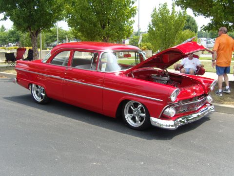 2007 Ford Mustang - Classic red 1956 Ford Fairlane sedan with custom wheels and open hood at an outdoor event.