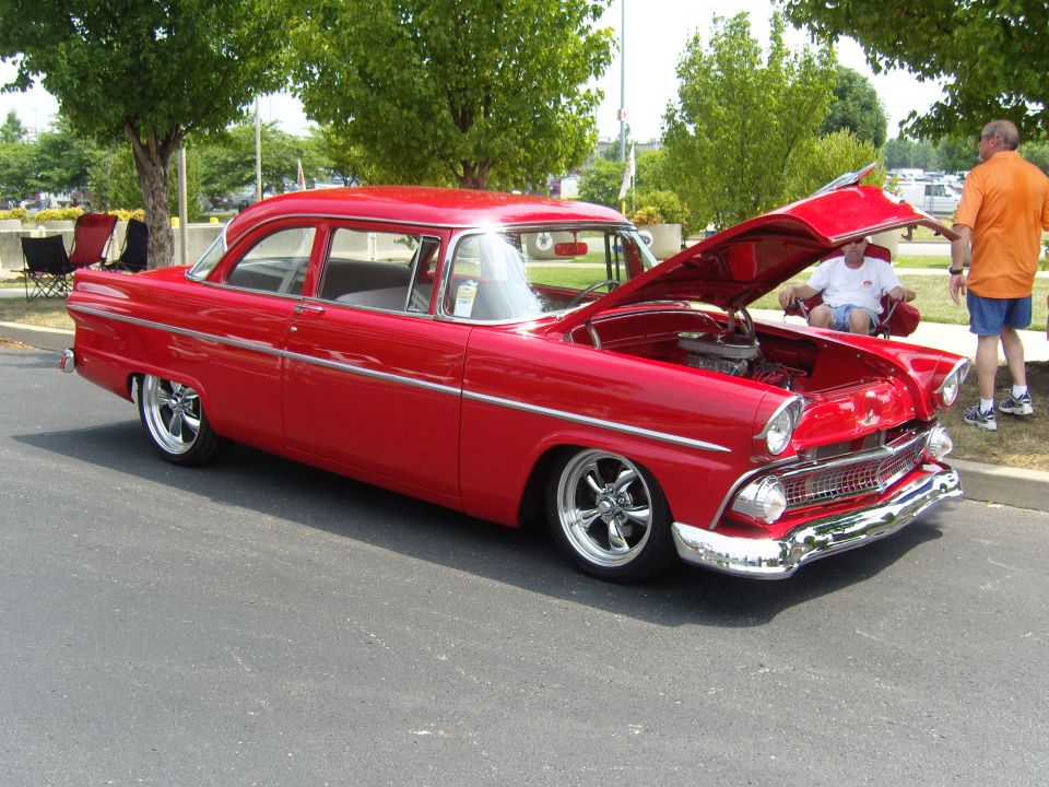 Red 1956 Ford Fairlane sedan, hood open showing engine, parked outdoors