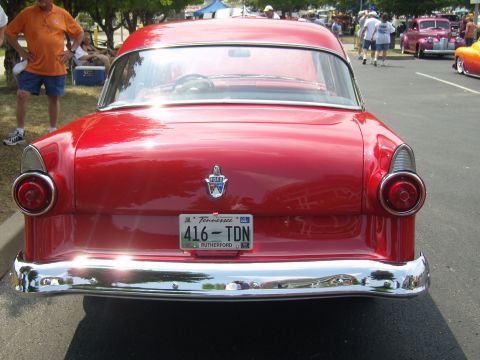 2007 Ford Mustang - A red classic car is parked at an outdoor event, with other vehicles and people in the background.