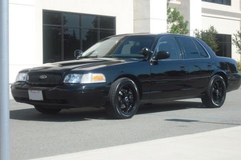 2003 Ford Crown Victoria - This black sedan is parked in front of a modern building with large windows.