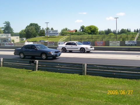 2003 Ford Crown Victoria - Two vehicles drive along a highway on a sunny day.