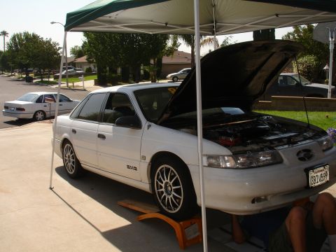 1993 Ford Taurus - Mechanic works on a 1993 Ford Taurus with its hood open, while another Taurus sits nearby.