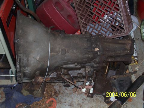 1990 Ford Bronco - A dirty, used automatic transmission is shown in a cluttered garage setting.