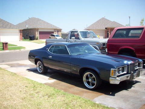1973 Mercury Cougar - A dark blue 1974 Mercury Cougar coupe is parked in a suburban driveway next to a pickup truck and a red SUV.