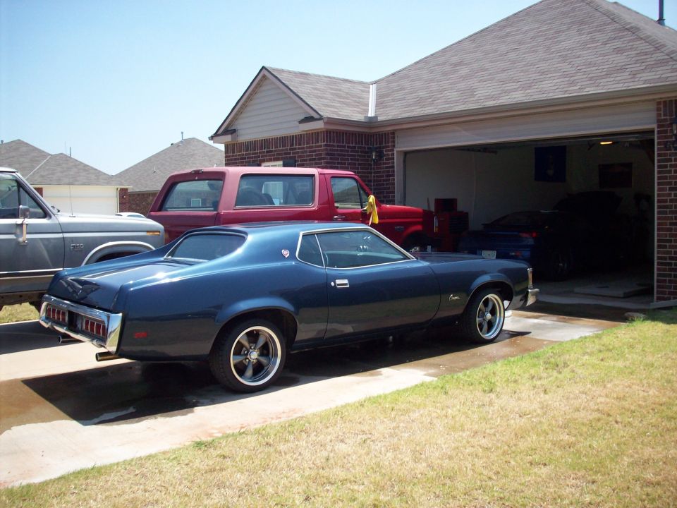 Dark blue 1973 Mercury Cougar coupe, side view, parked in driveway with other vehicles