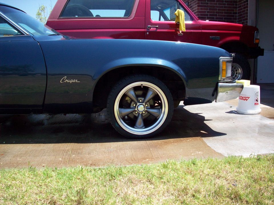 Dark blue Mercury Cougar front fender with Cougar script badge and gray five-spoke wheel
