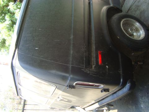 1986 Ford Bronco - A dusty black van is viewed from the side, showing its rear wheel and a red reflector.