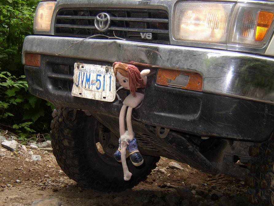 Front of dark Toyota V6 truck with BC plate JVM 511 and a rag doll hanging on the bumper, on a dirt trail