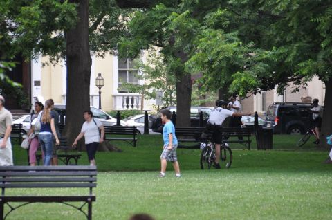 1996 Ford Bronco - A park scene with pedestrians, parked cars, and a police officer on a bicycle.