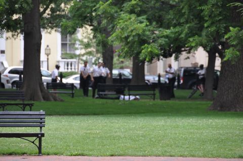 1996 Ford Bronco - Police officers are gathered in a park around a person lying on the grass near benches.
