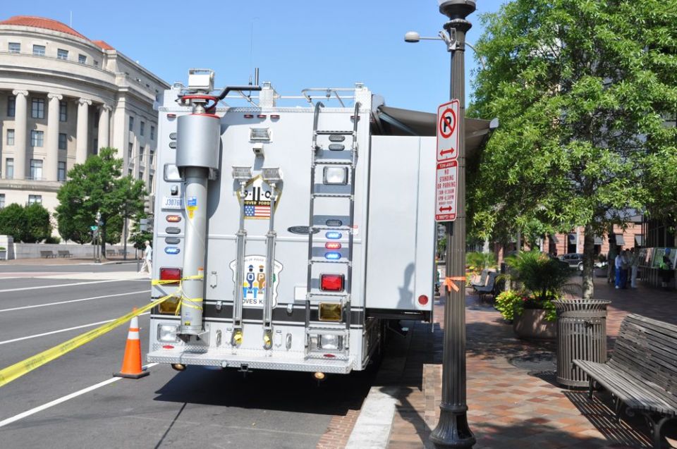 Rear view of a white specialized truck with ladders, yellow caution tape, and an orange cone
