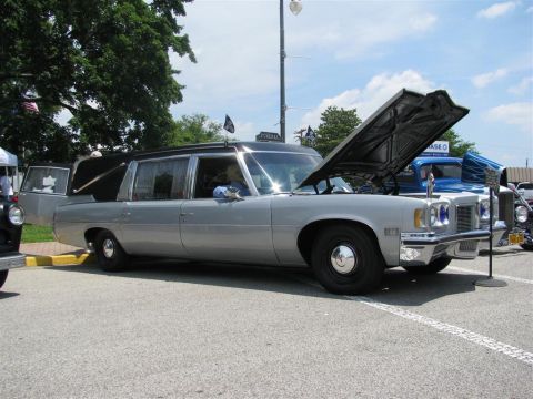 2003 Mercury Marauder - A silver hearse is displayed with its hood open at a car show, alongside other vehicles.