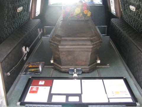 2003 Mercury Marauder - The interior of a hearse holds two coffins, one adorned with flowers, alongside a display of documents.
