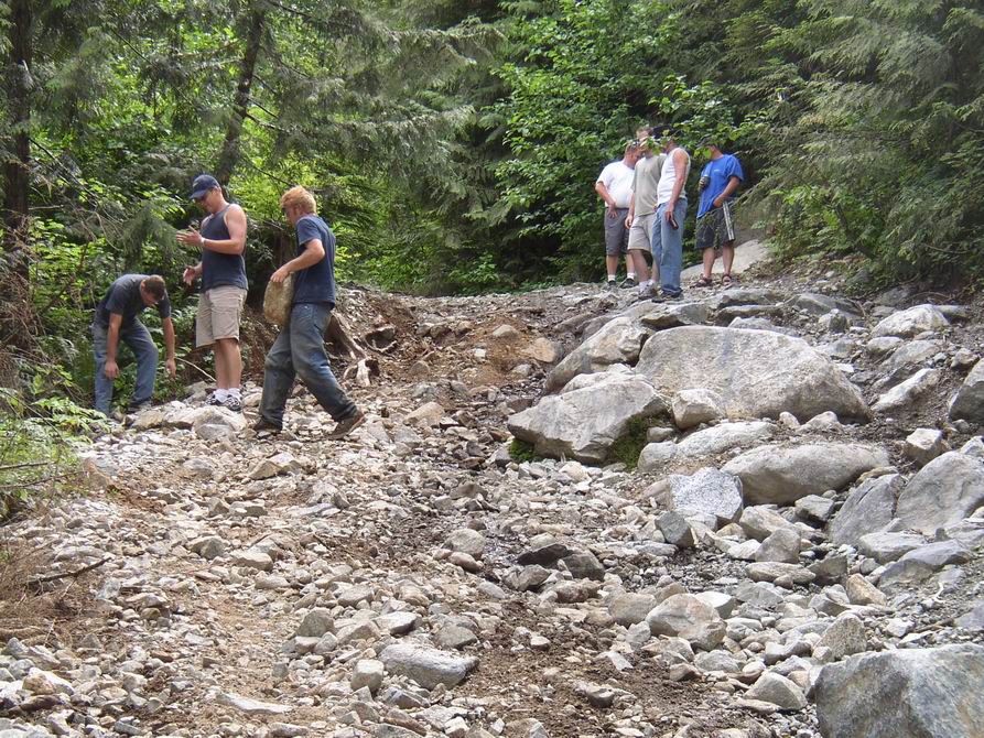 Group of men standing on a rocky washed-out forest trail strewn with boulders and gravel