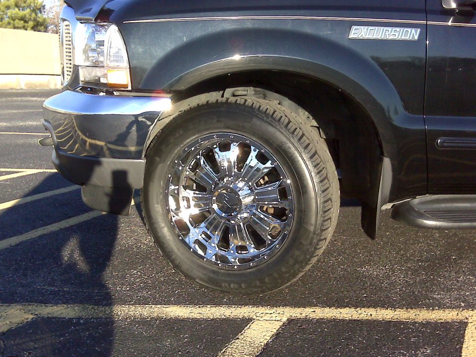 Dark Ford Excursion front wheel with chrome wheel and all-terrain tire, parked on asphalt