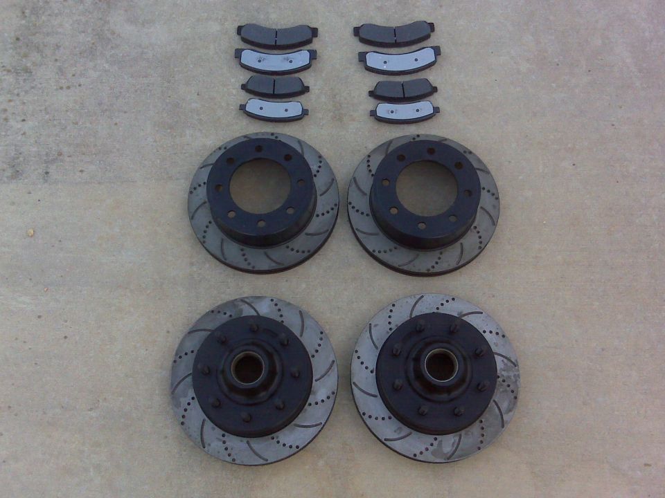 Four drilled and slotted brake rotors and brake pad sets laid out on concrete