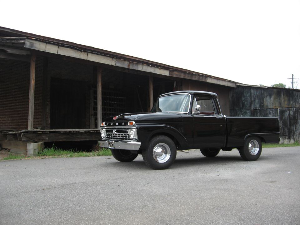 Black 1966 Ford F-100 pickup truck parked in front of an old building