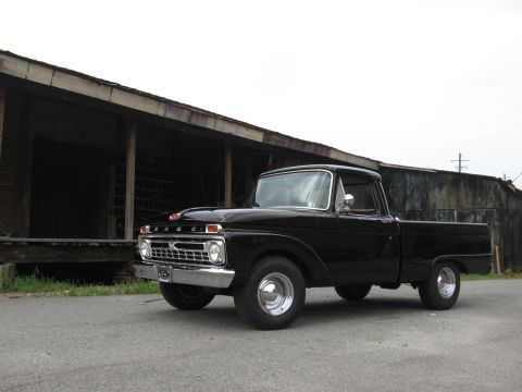 1966 Ford F-100 - A classic black Ford F-100 pickup truck is parked in front of an old wooden structure.