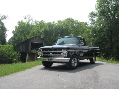 1966 Ford F-100 - A black 1965 Ford F-100 pickup truck is parked on a road with a covered bridge behind it.