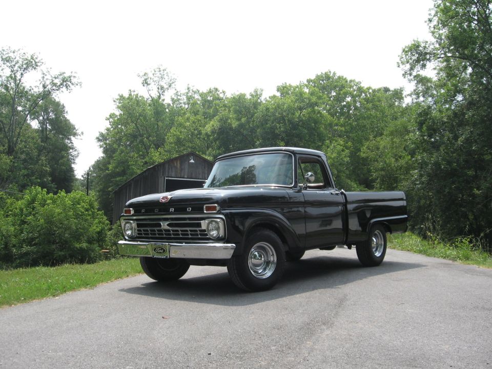 Gloss black Ford styleside pickup on a country road with a barn behind, chrome grille and wheels