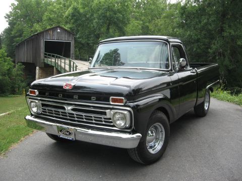 1966 Ford F-100 - A classic black Ford pickup truck is parked on a paved road, with a wooden covered bridge visible behind it.