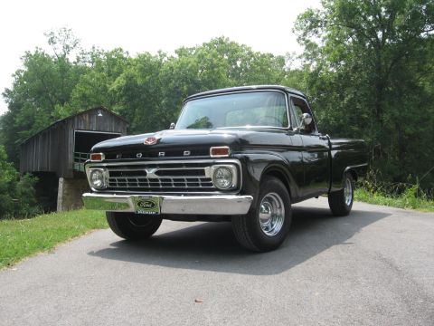 1966 Ford F-100 - This black 1966 Ford F-100 pickup truck is parked on a paved road next to a wooden covered bridge.