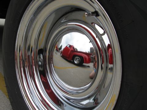 1966 Ford F-100 - A shiny hubcap reflects a red pickup truck parked on a street.