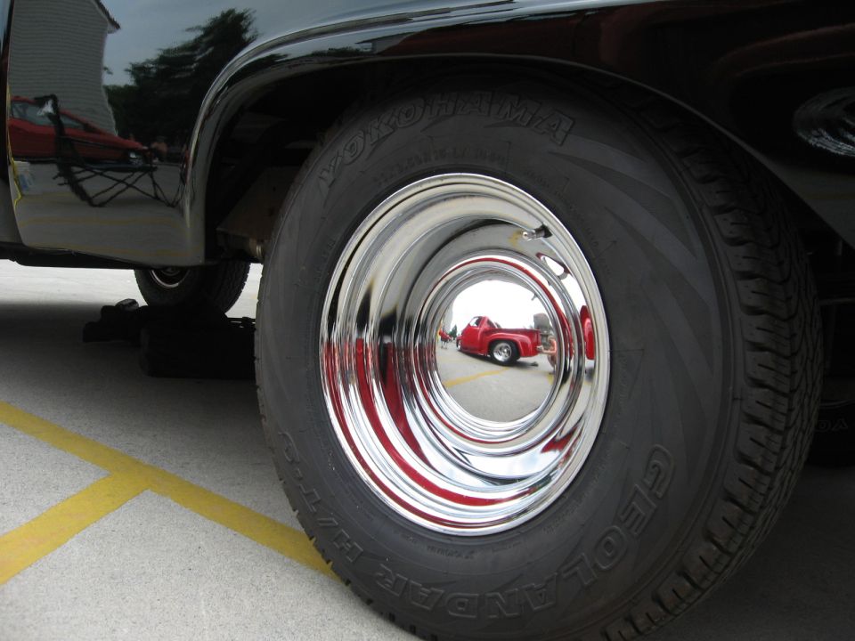 Black pickup truck's chrome wheel and Yokohama tire, reflecting a red pickup truck