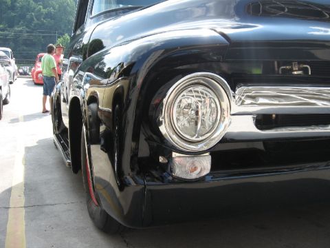 1966 Ford F-100 - Low angle view of a black pickup truck's front end with chrome accents and a visible red wheel trim.