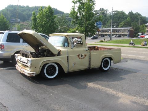 1966 Ford F-100 - This vintage Ford F-100 pickup truck, likely a 1956 model, is parked with its hood raised, revealing the engine and a glimpse of the interi…